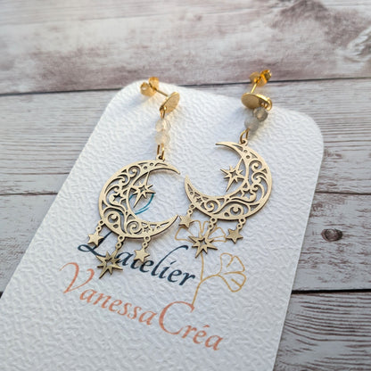 Paire de boucles d'oreilles artisanales motif lune, étoiles et labradorite posées sur le support de présentation de l'atelier.