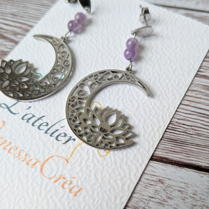 Vue de biais des boucles d'oreilles lune et lotus argentées sur le support de présentation.