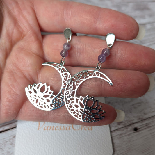 Paire de boucles d'oreilles lune et lotus argentées en acier inoxydable tenue en main.