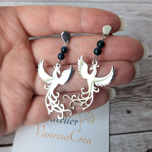 Paire de boucles d'oreilles phénix argentées en acier inoxydable tenue en main.