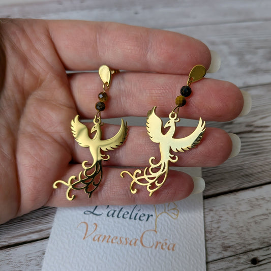 Paire de boucles d'oreilles phénix dorées en acier inoxydable tenue en main.