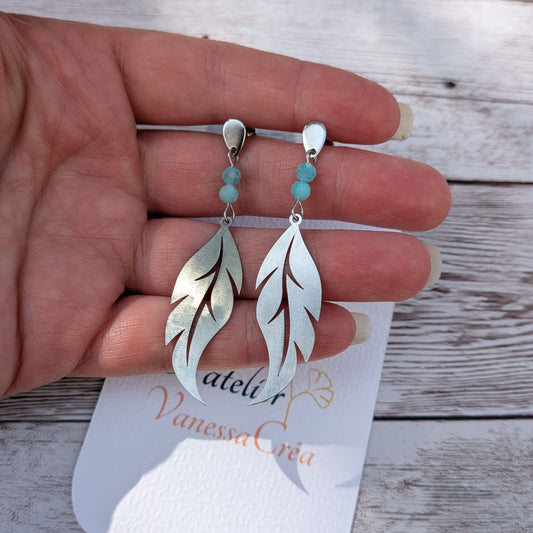 Boucles d'oreilles plume ajourée en acier inoxydable avec perles facettées d'amazonite de 4 mm, présentées sur la main avec la carte de l'atelier Vanessa Créa.