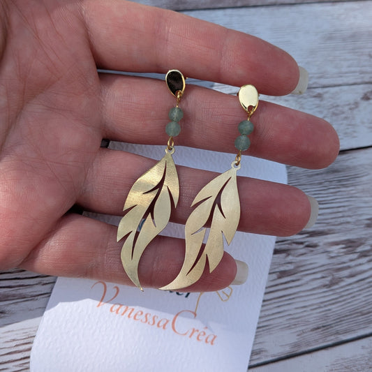 Boucles d'oreilles plume ajourée en laiton avec perles facettées d'aventurine, présentées sur la main avec la carte de l'atelier Vanessa Créa.