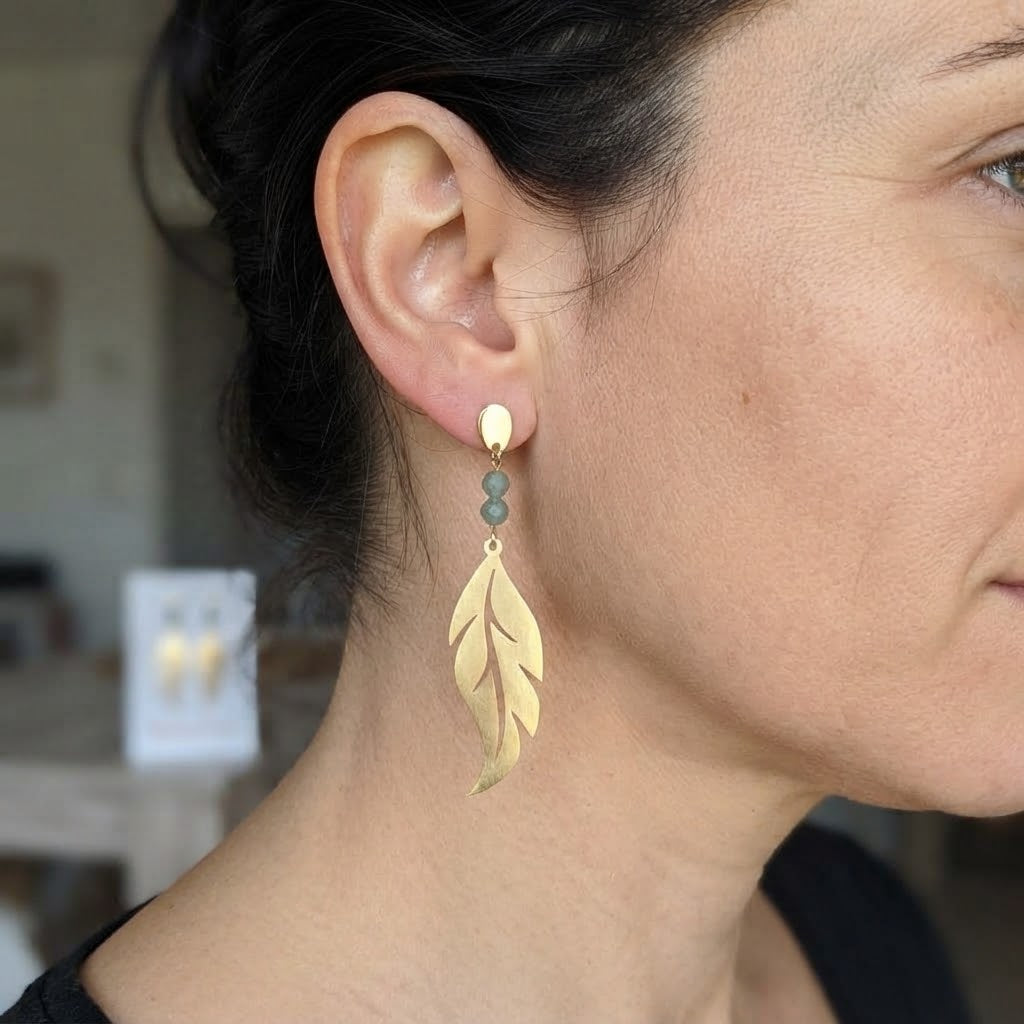 Boucles d'oreilles plume ajourée en laiton et aventurine portées, mettant en valeur leur élégance et leur éclat doré.