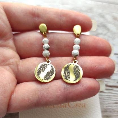 Boucles d'oreilles plume dorées en acier inoxydable tenues délicatement dans la main.