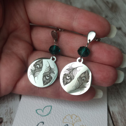 Boucles d'oreilles pendantes en acier inoxydable poli miroir avec gravure laser de deux plumes de paon et cristal à facettes.