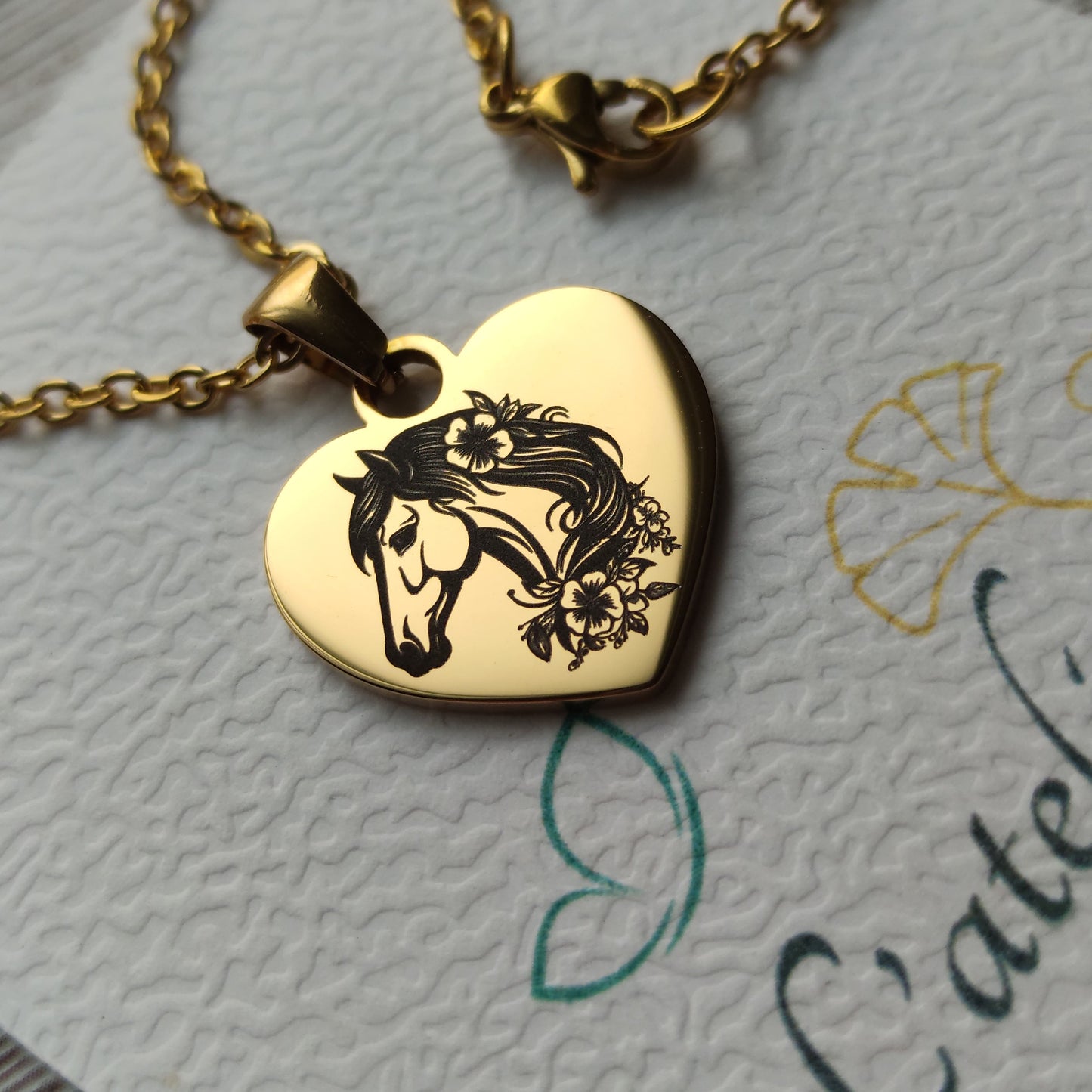 Collier pendentif cœur en acier poli miroir avec gravure tête de cheval et fleurs de profil.