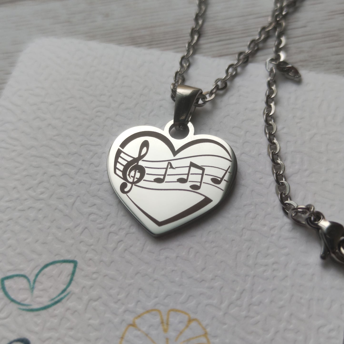 Collier pendentif cœur en acier inoxydable avec gravure de partition et notes de musique, finition poli miroir.