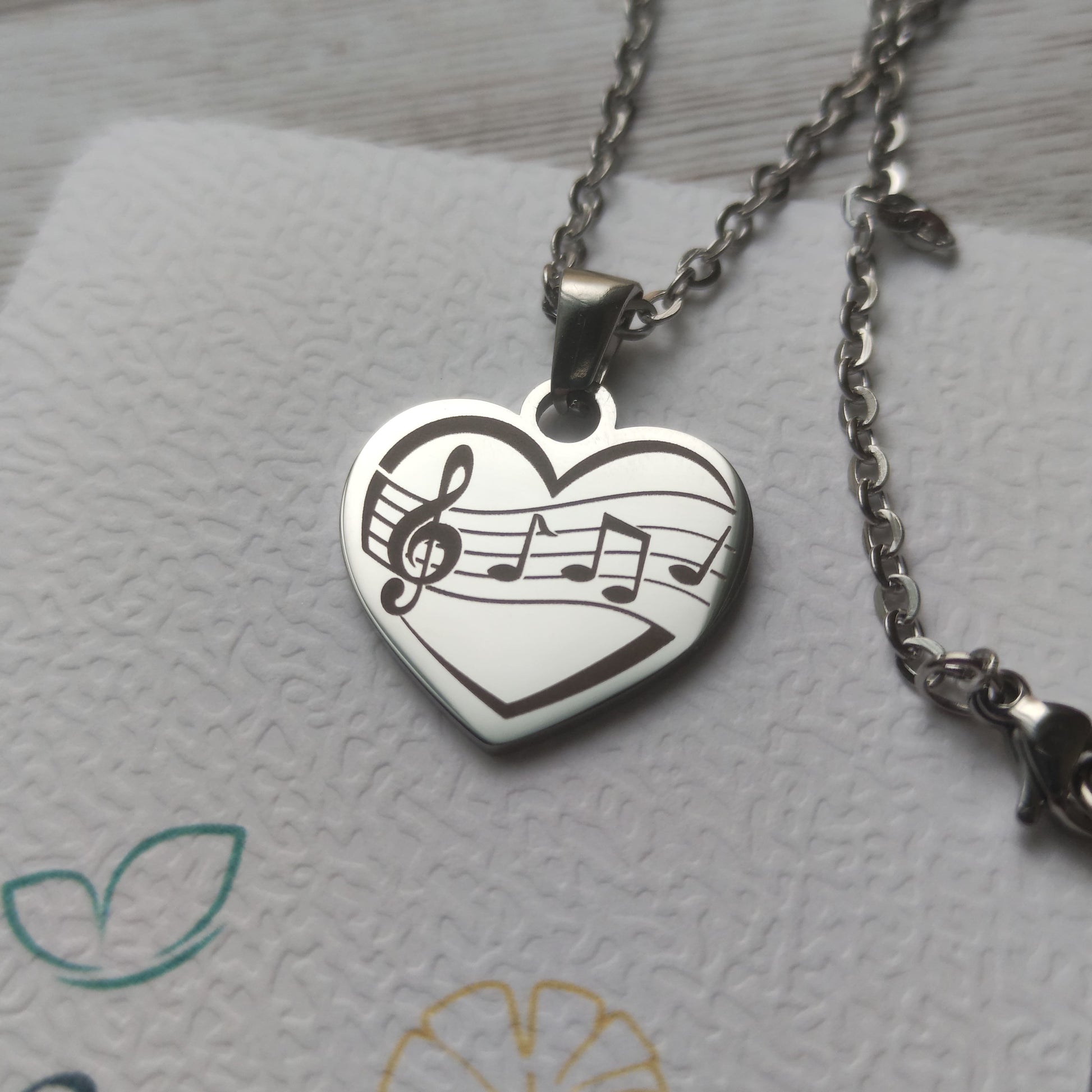 Collier pendentif cœur en acier inoxydable avec gravure de partition et notes de musique, finition poli miroir.