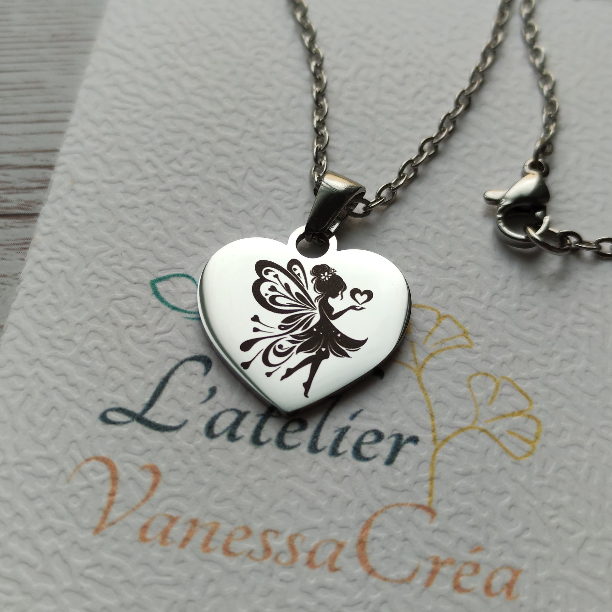 Collier en acier inoxydable poli avec pendentif cœur de 2,5 cm gravé d'une fée envoyant des cœurs.