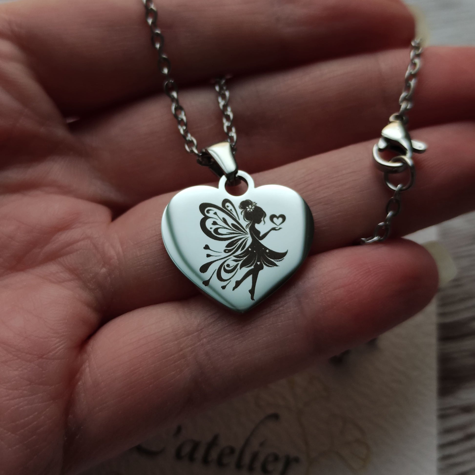 Collier en acier inoxydable poli avec pendentif cœur de 2,5 cm gravé d'une fée envoyant des cœurs.
