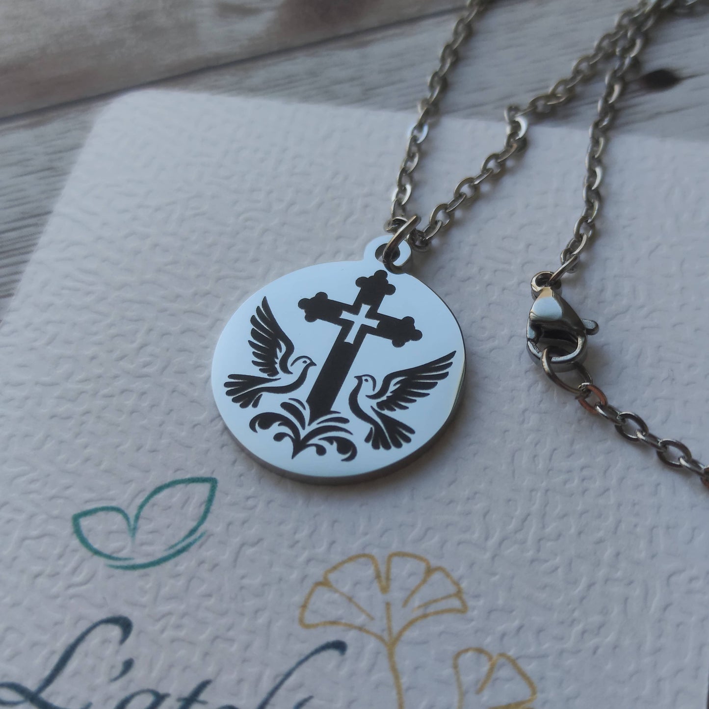 Pendentif rond poli miroir en acier inoxydable avec gravure de précision d'une croix entourée de deux colombes.
