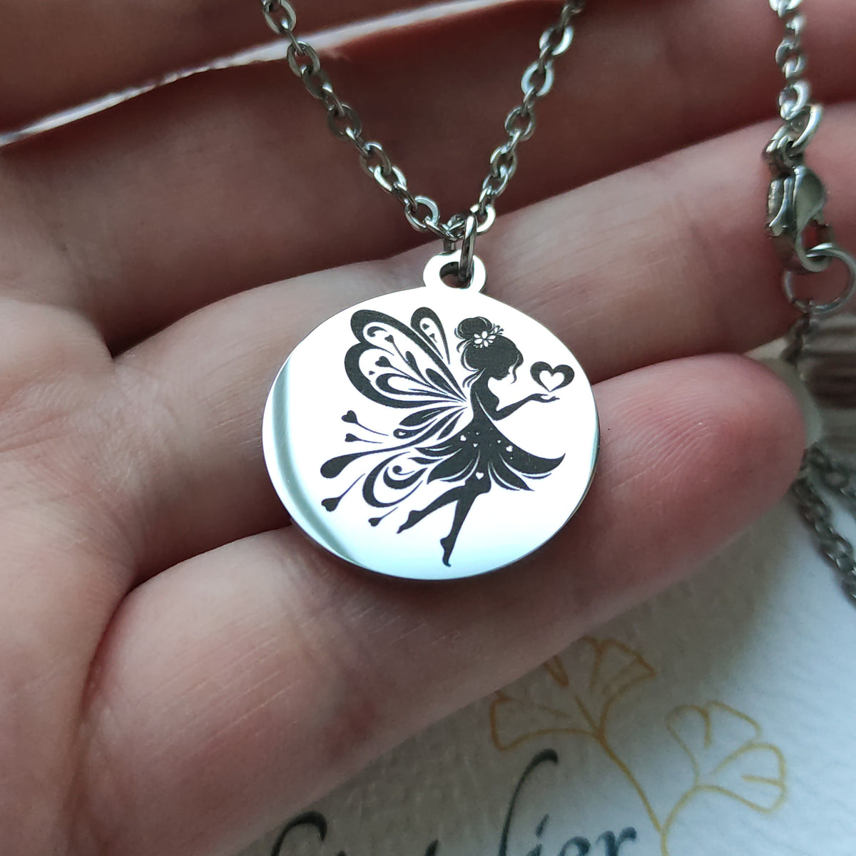Collier pendentif rond en acier inoxydable poli miroir avec gravure laser d'une fée et de cœurs.