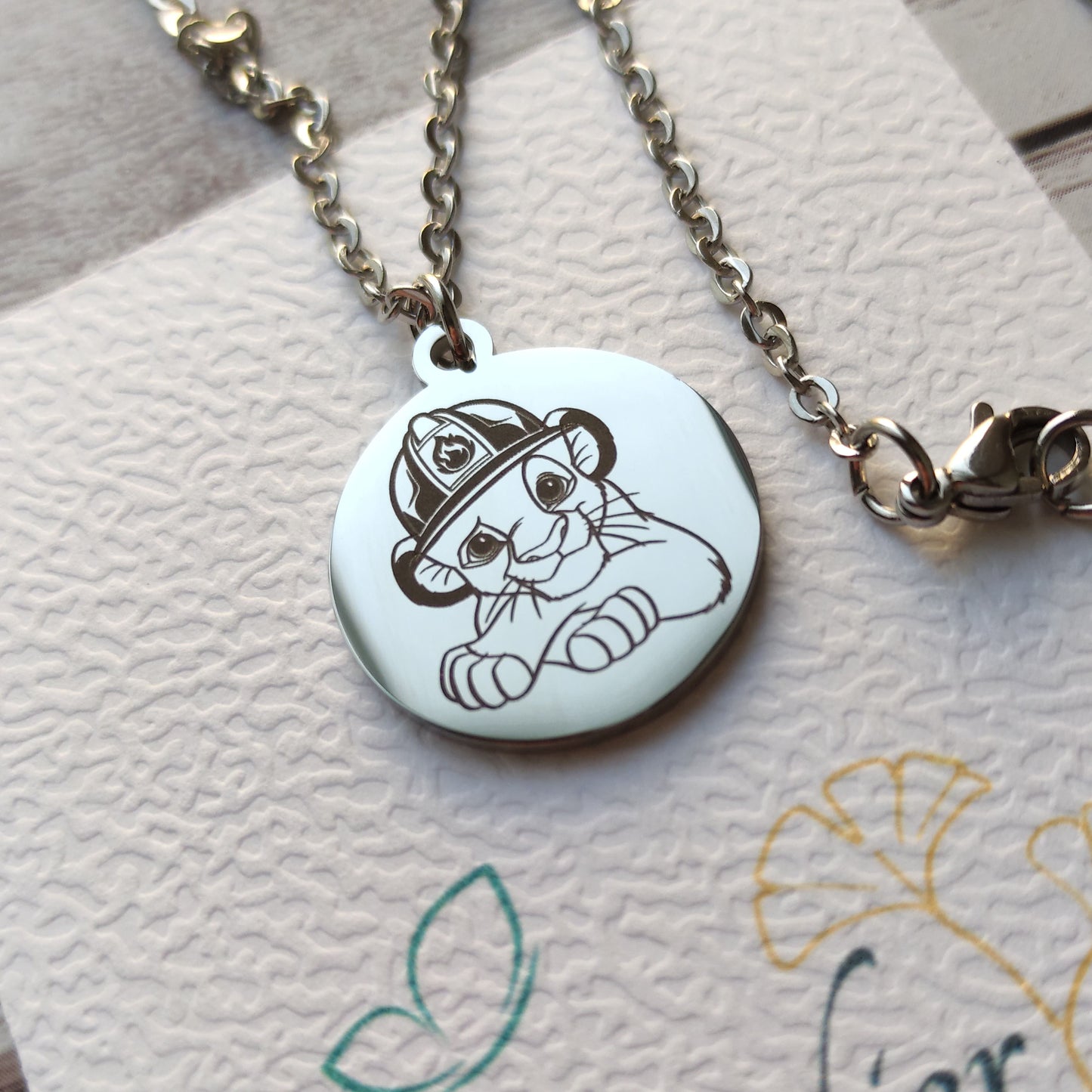 Collier médaille ronde en acier poli miroir avec gravure de Simba portant un casque de pompier.