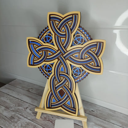 Croix celtique artisanale en bois 5 couches, motifs entrelacs bleus et bois, présentée sur un chevalet.