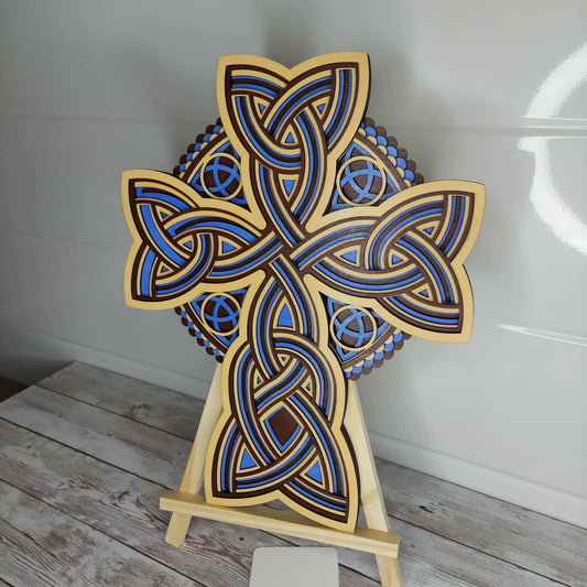 Croix celtique artisanale en bois 5 couches, motifs entrelacs bleus et bois, présentée sur un chevalet.