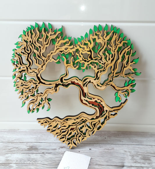 Décoration murale artisanale Arbre de Vie en forme de cœur, réalisée en 5 couches de bois de tilleul avec des détails de feuilles vertes.