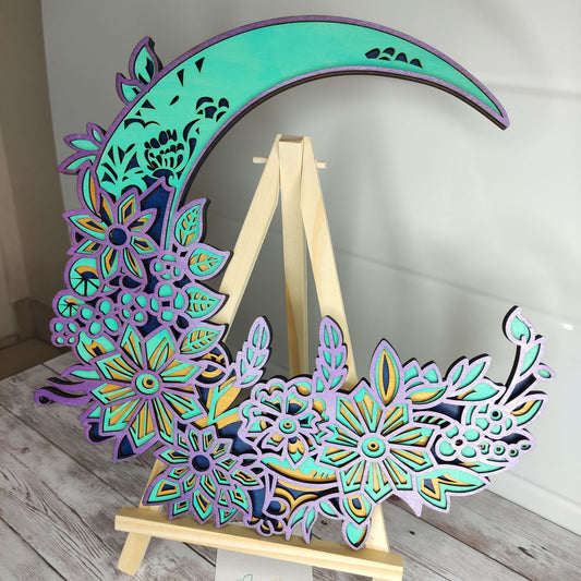 Décoration murale ronde Lune Fleurie en bois de tilleul, finition artisanale bleu turquoise et violet, présentée sur un chevalet en bois.