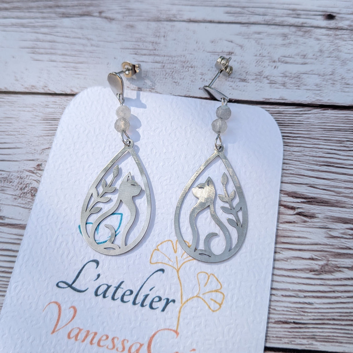 Gros plan sur les détails de découpe des boucles d'oreilles chat ajouré en acier et les perles de labradorite.