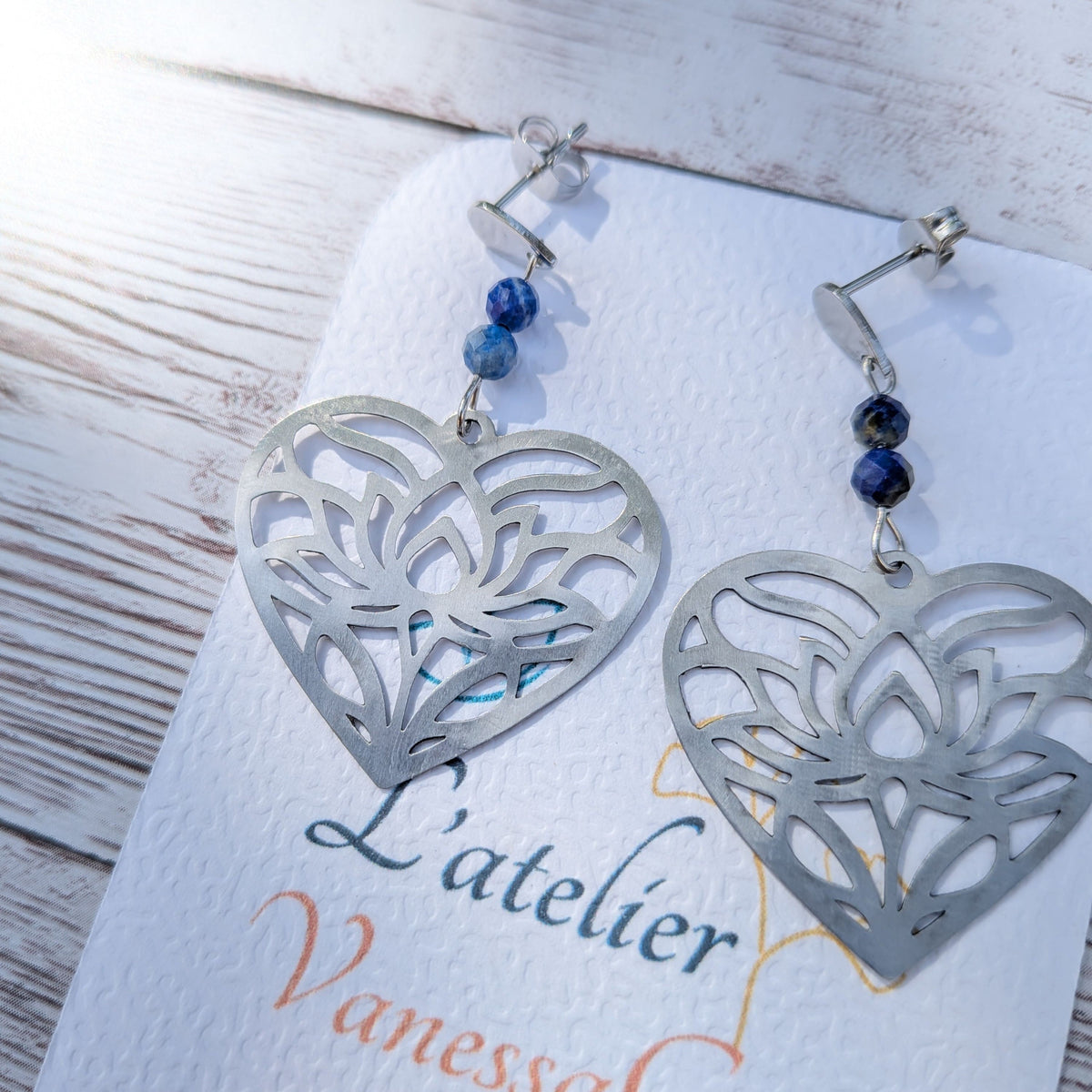 Gros plan sur les finitions des boucles d'oreilles cœur ajouré en acier et les perles facettées de lapis-lazuli.