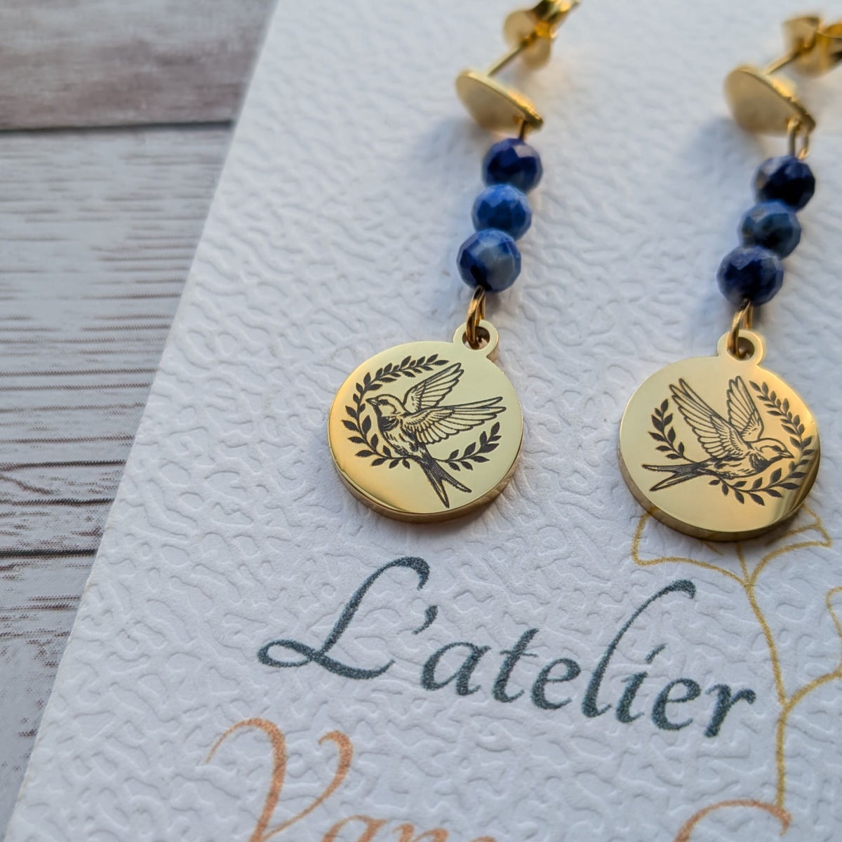 Gros plan sur le médaillon gravé motif hirondelle et les perles bleues des boucles d'oreilles artisanales Vanessa Créa.