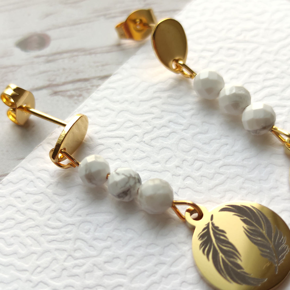 Gros plan sur le médaillon gravé motif plume des boucles d'oreilles artisanales Vanessa Créa.