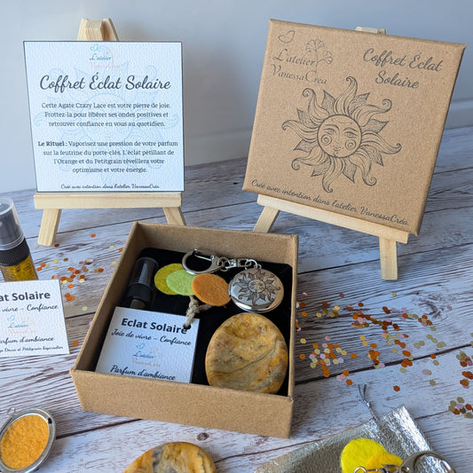 Gros plan sur l'intérieur du coffret Éclat Solaire ouvert, montrant la feutrine jaune et orange, le flacon de parfum et la carte explicative en arrière-plan.