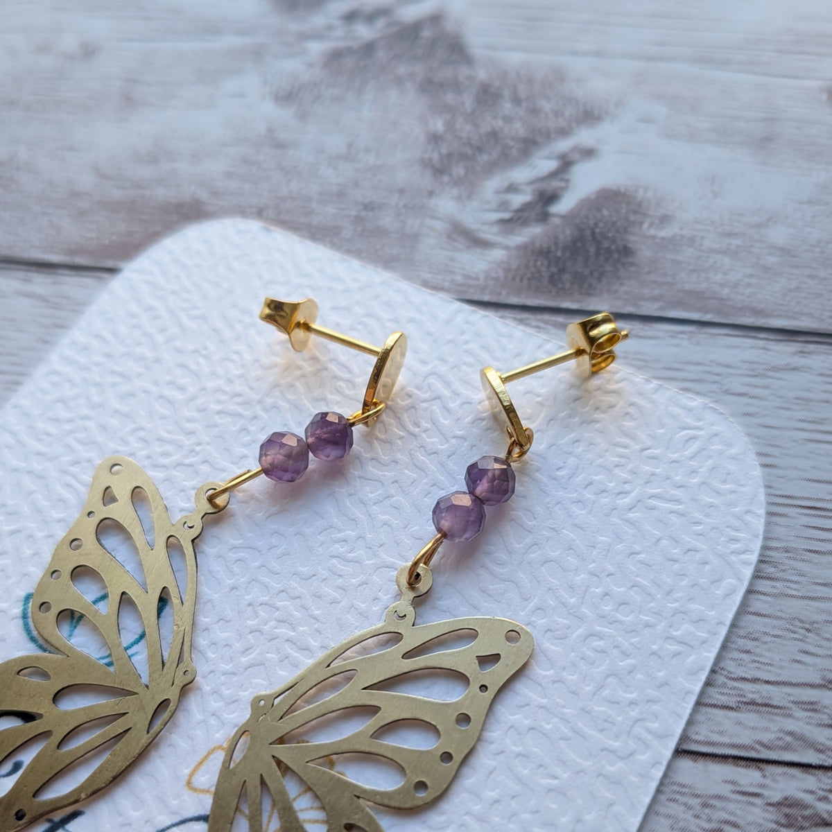 Détail des attaches et des finitions polies des boucles d'oreilles papillon artisanales en laiton protégé.