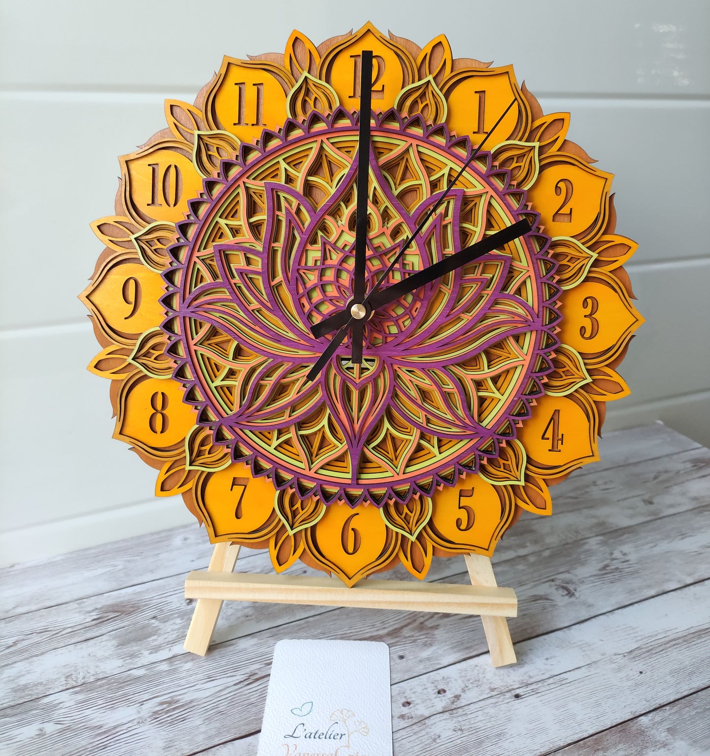 Horloge murale artisanale mandala fleur de lotus en bois 7 couches, avec mécanisme à quartz silencieux, présentée sur un chevalet.