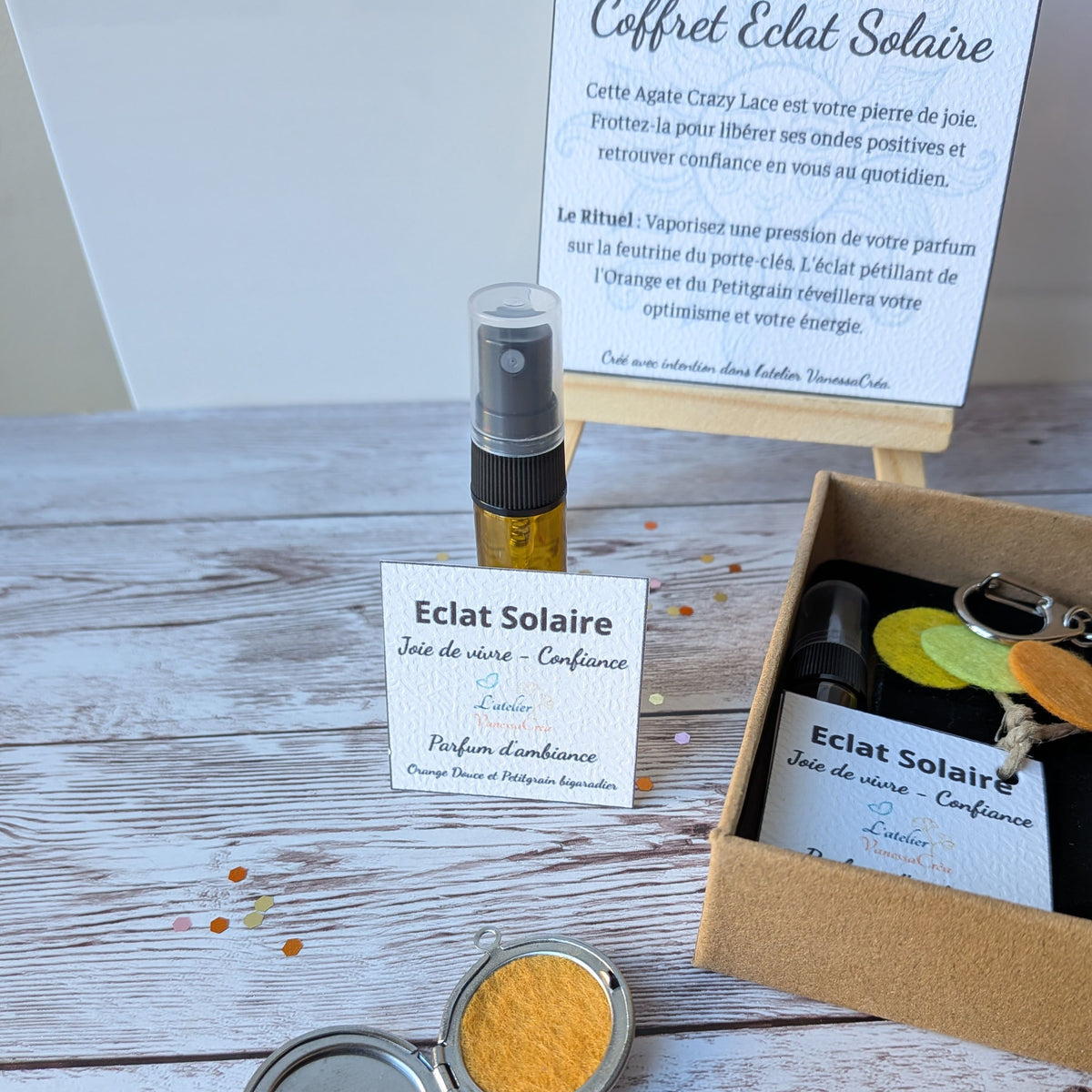 Focus sur le flacon de parfum d'ambiance bio, le médaillon porte-clés ouvert avec feutrine jaune et le galet d'agate crazy lace du coffret Éclat Solaire.