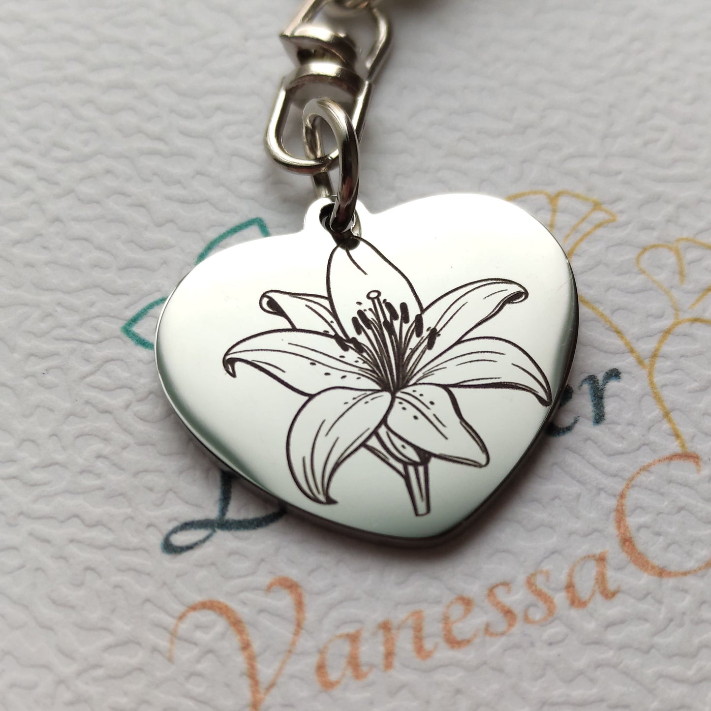 Porte-clés en forme de cœur en acier inoxydable poli miroir avec gravure laser d'une fleur de lys et texte personnalisé.