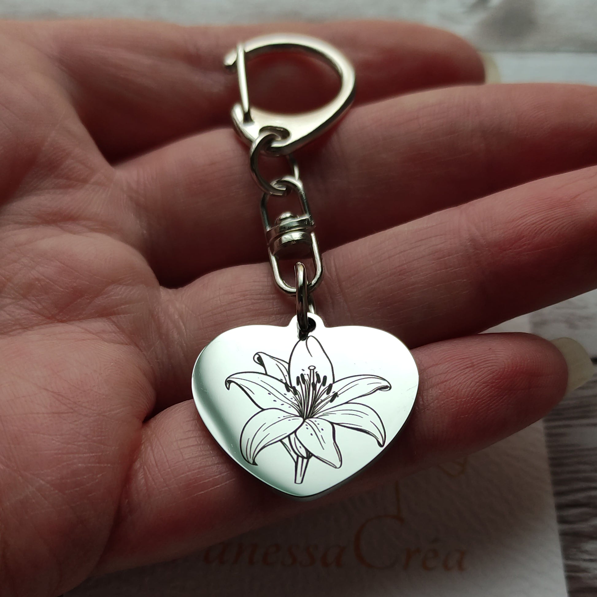 Porte-clés en forme de cœur en acier inoxydable poli miroir avec gravure laser d'une fleur de lys et texte personnalisé.