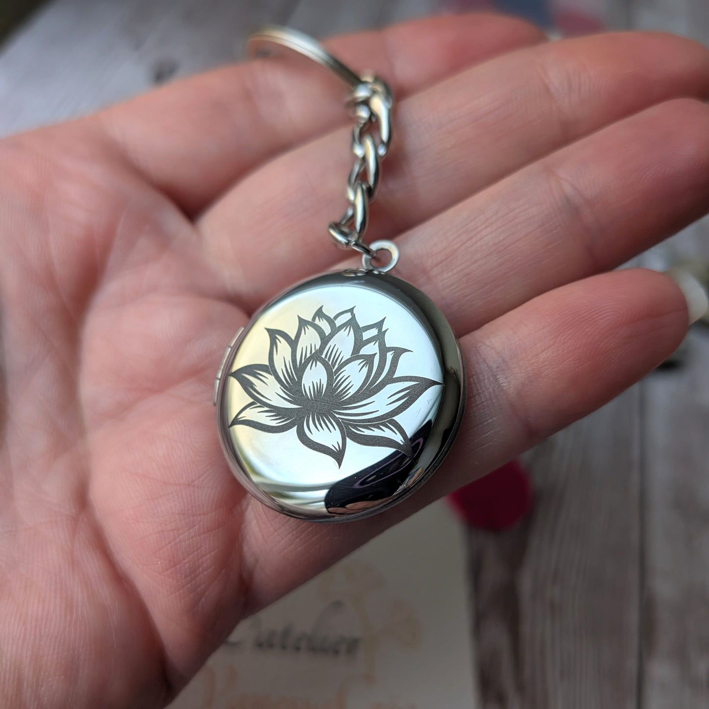 Présentation en main du porte-clés olfactif en acier inoxydable avec gravure de la Fleur de Lotus, issu du coffret Sérénité.