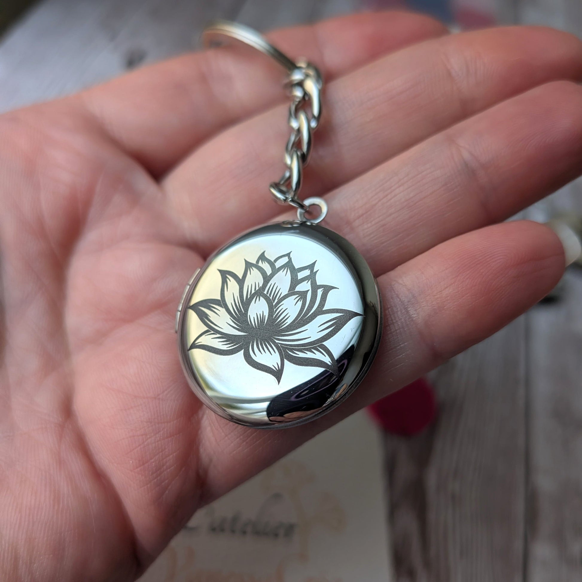 Présentation en main du porte-clés olfactif en acier inoxydable avec gravure de la Fleur de Lotus, issu du coffret Sérénité.