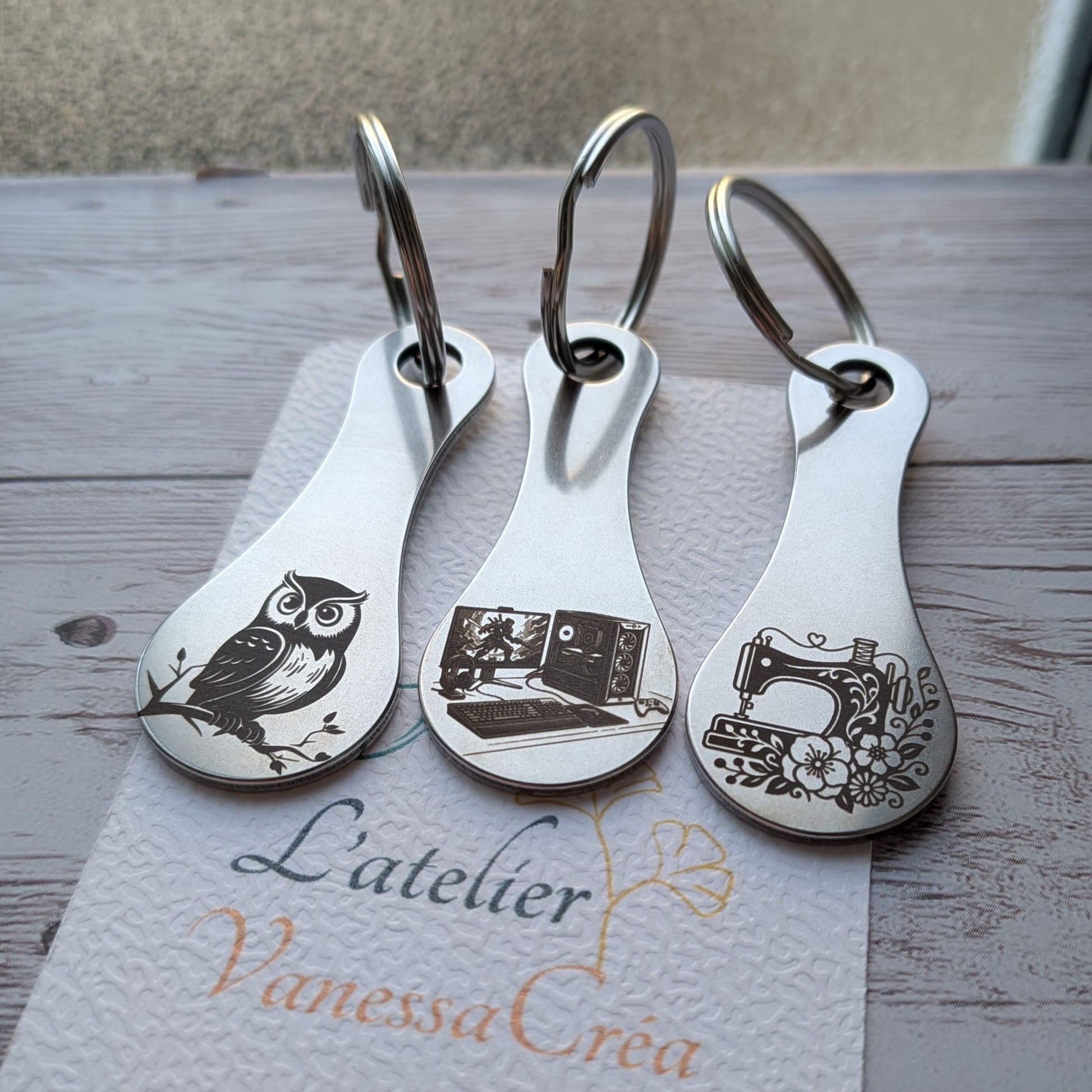 Trois porte-clés jetons de caddie en acier inoxydable avec gravures laser : une chouette, un ordinateur gamer et une machine à coudre.