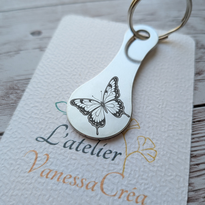 Porte-clés jeton de caddie en acier inoxydable gravé d'un motif papillon délicat, présenté sur son support L'Atelier VanessaCréa.